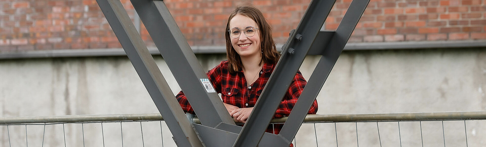 Eine Frau lächelt freundlich in die Kamera während sie sich an einem Stahlpfeiler anlehnt