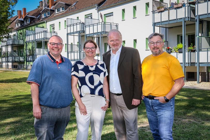 Drei Männer und eine Frau stehen in einem begrünten Innenhof vor modernisierten Mehrparteienhäusern.
