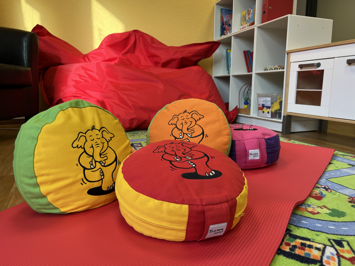 In einer Kinderspielecke liegen eine Yogamatte und mehrere Yogakissen.