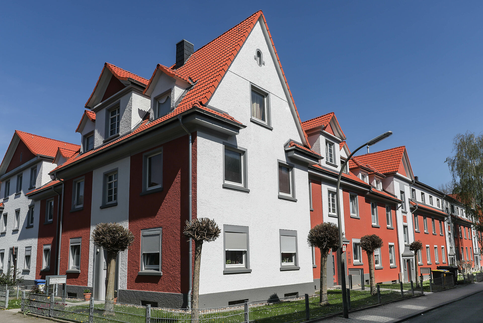 Weiß und rot gestrichene Altbauhäuser mit Giebeldächern und grünem Vorgarten