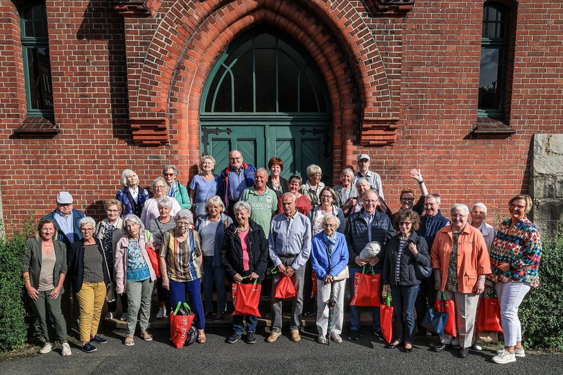Mieterinnen und Mieter sowie Mitarbeiterinnen des Wohnungsunternehmens DOGEWO21 stehen auf den Treppenstufen vor einem historischen grünen Holzeingang auf der Zeche Zollern und schauen freundlich in Richtung des Fotografen.