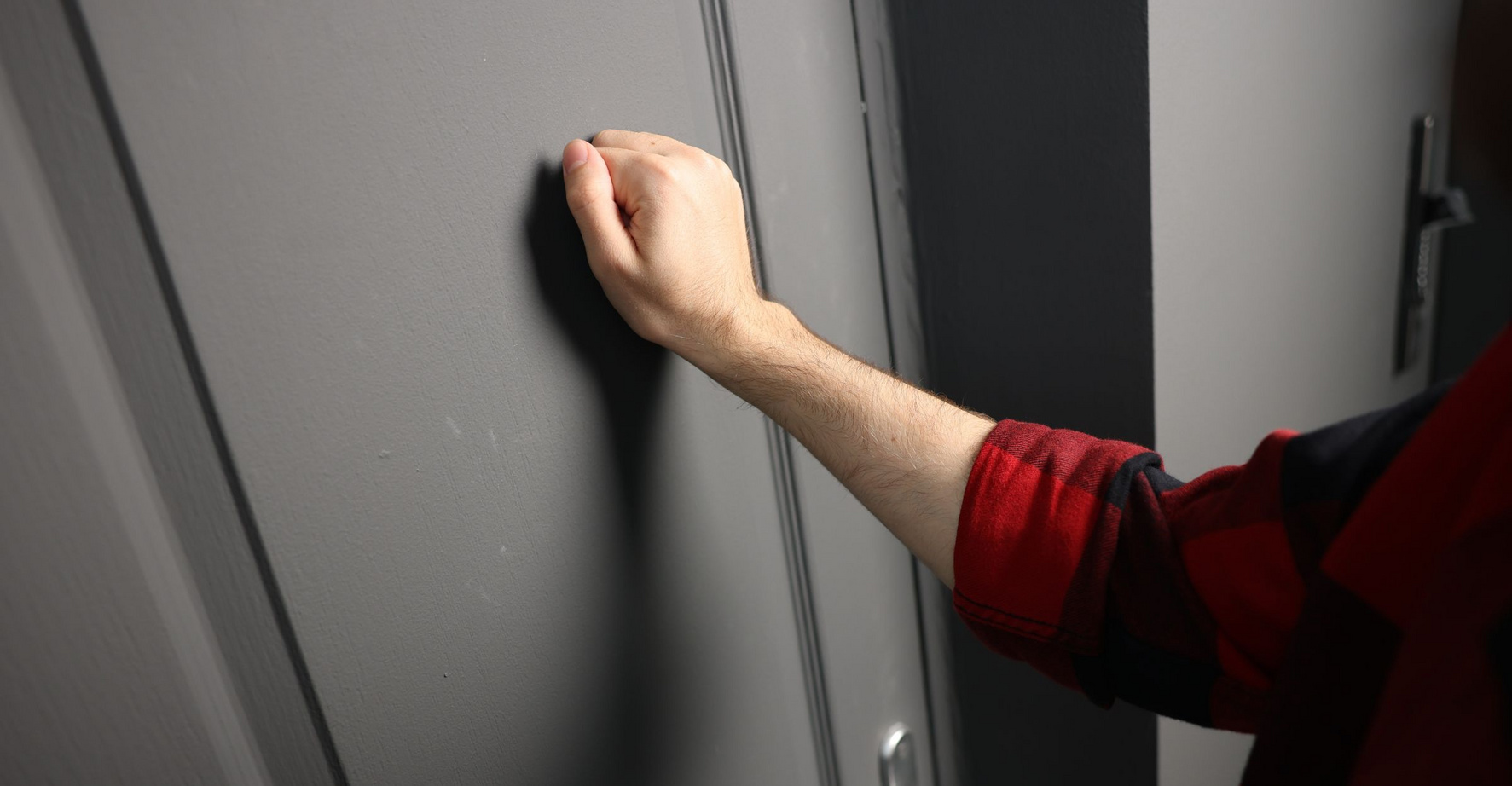 Eine Person klopft an eine graue Wohnungstür