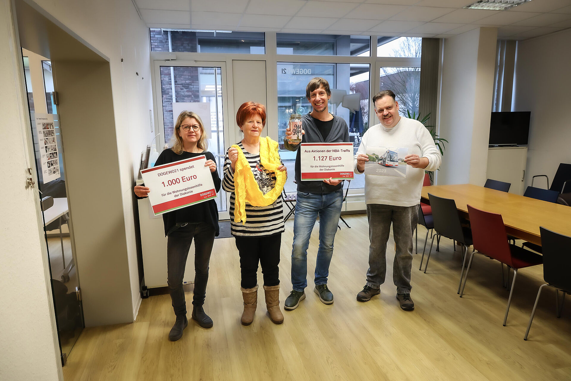 Menschen bei der Übergabe von zwei symbolischen Spendenschecks in einer DOGEWO21-Nachbarschaftsagentur