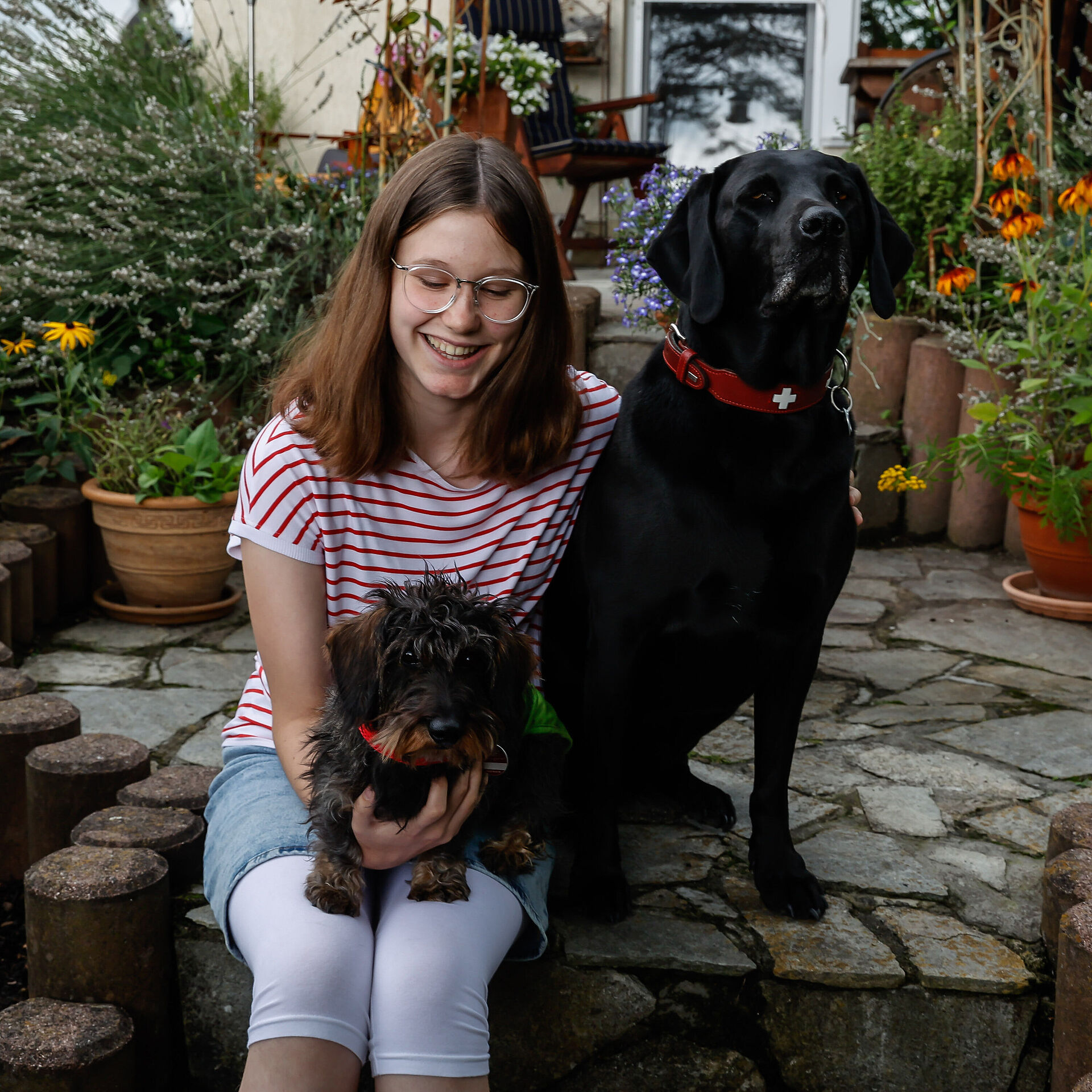Mädchen sitzt mit zwei Hunden auf einer Steinstufe und lächelt