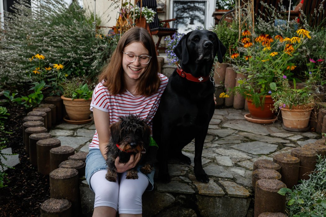 Mädchen sitzt mit zwei Hunden auf einer Steinstufe und lächelt