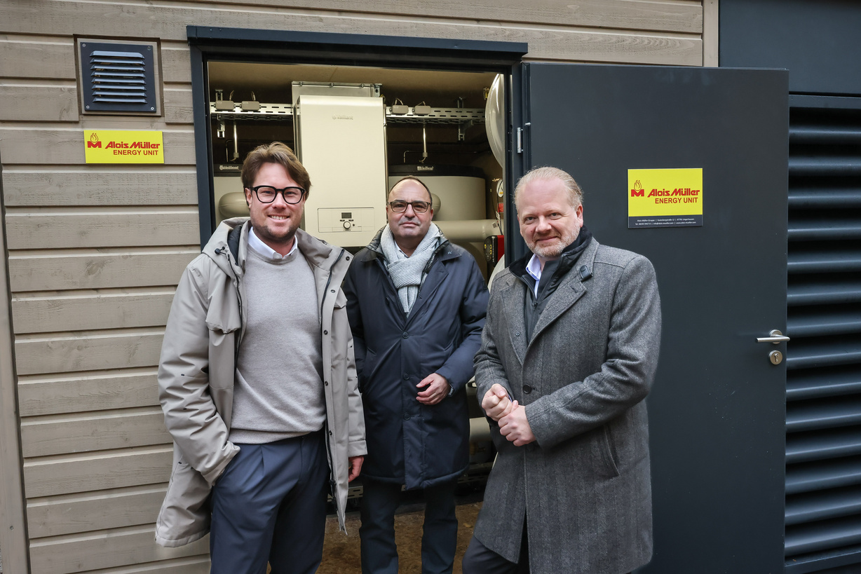 Drei Männer stehen vor der offenen Tür einer Container-Heizzentrale.