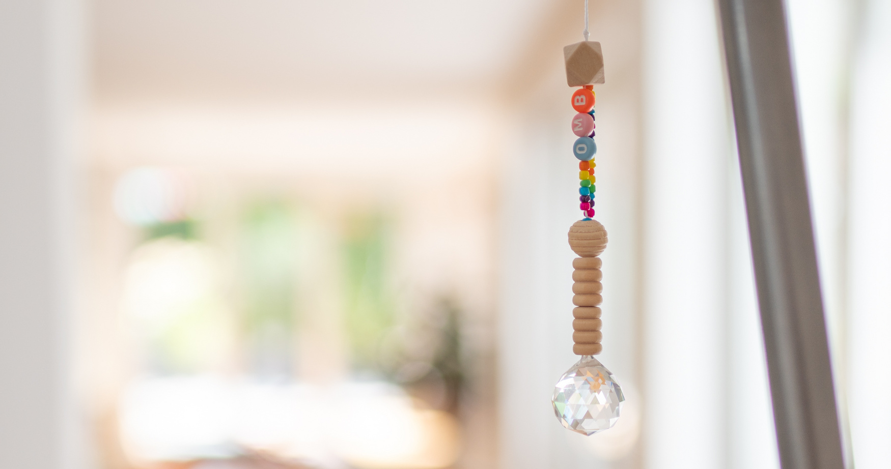 Ein Lichtfänger, der aus Holzperlen und bunten Perlen besteht und im Fenster hängt.