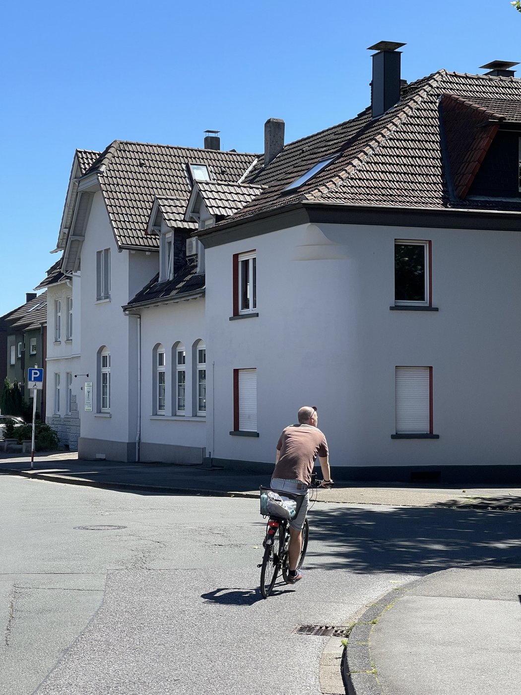 Fahrradfahrer biegt rechts vor einem weißen Haus ab 