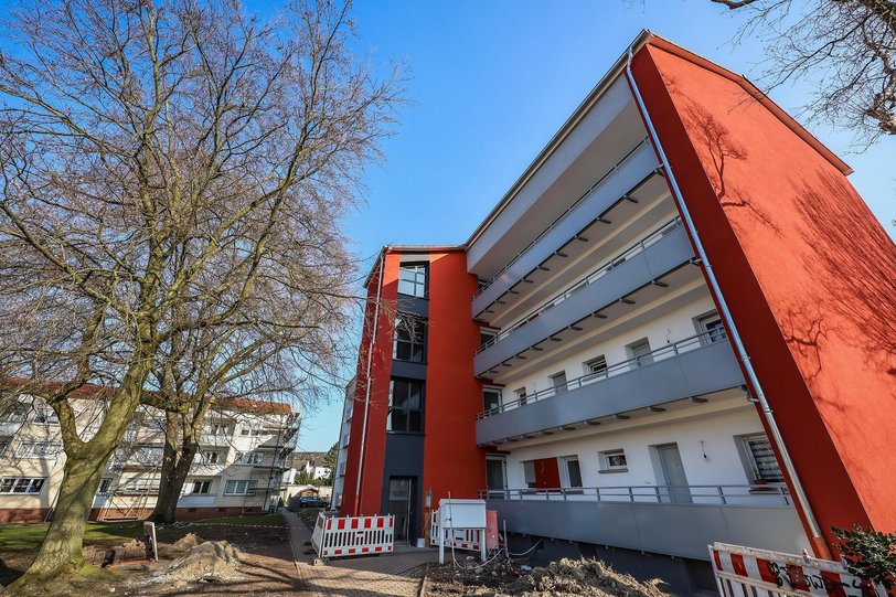 Ein modernisiertes Mehrfamilienhaus in rot und antrazith mit einem Baum und Baustellenbarken vor der Tür.