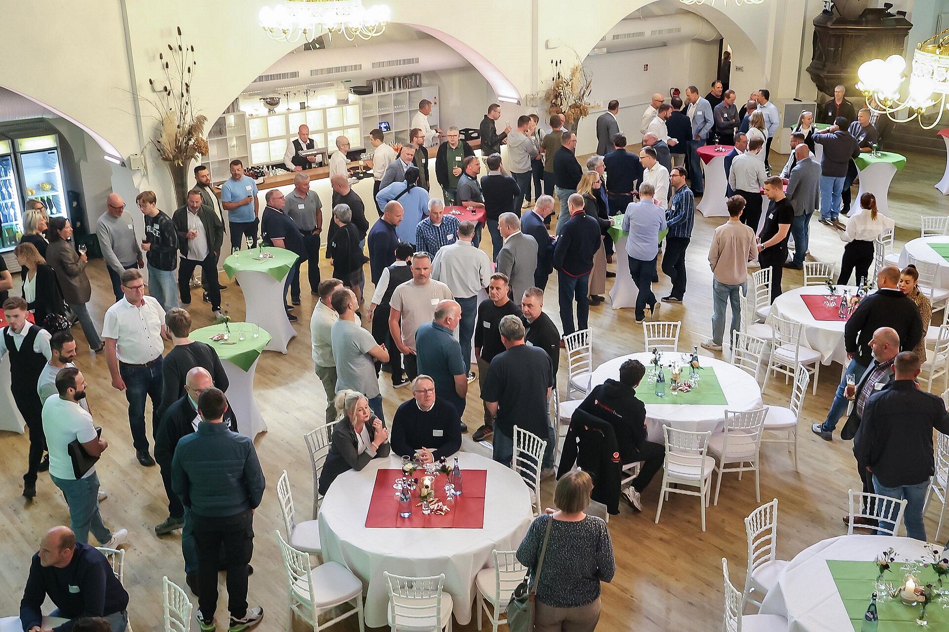Viele Männer und Frauen stehen und sitzen in gemütlicher Atmosphäre in einer Eventkirche und unterhalten sich.