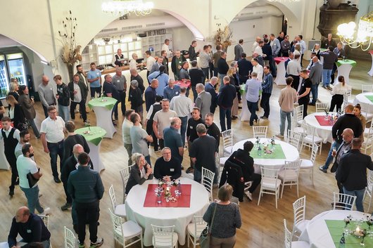 Viele Männer und Frauen stehen und sitzen in gemütlicher Atmosphäre in einer Eventkirche und unterhalten sich.