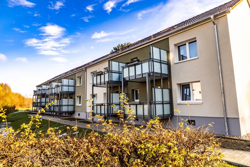 Drei modernisierte Mehrfamilienhäuser mit verputzter Wärmedämmung und mit großen Vorstellbalkonen ist umgeben von Bü+schen und Bäumen unter einem strahlend blauen Himmel