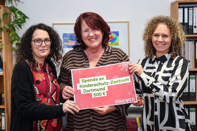 3 Frauen zeigen eine Spende Richtung Fotografen