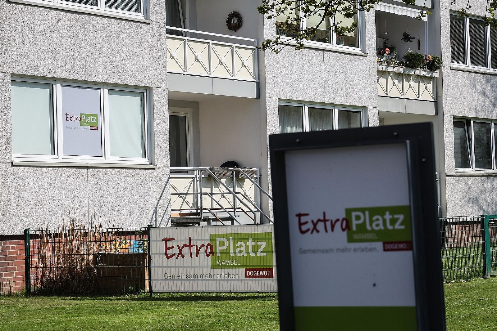Ein Mehrfamilienhaus mit mehreren Balkonen und Schilder, die auf den ansässigen Nachbarschaftstreff hinweisen.