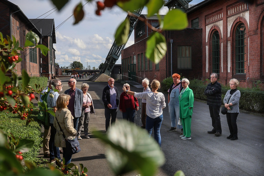 Männer und Frauen gehen über das Gelände der Zeche Zollern, im Hintergrund sind die alten Gebäude zu sehen.