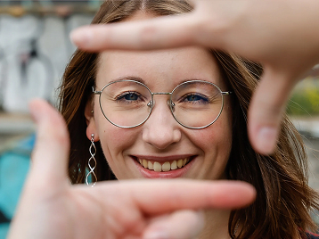Lächelnde Frau im Hintergrund. Im Vordergrund sind die Hände unscharf erkennbar.